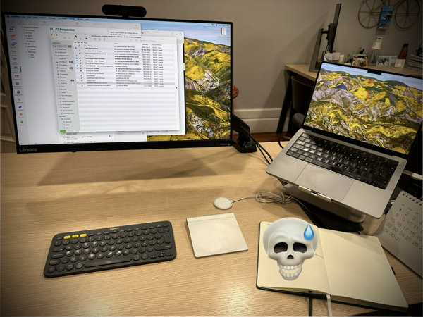 Escritorio con ordenador portátil, pantalla grande, teclado, trackpad y cuaderno. 